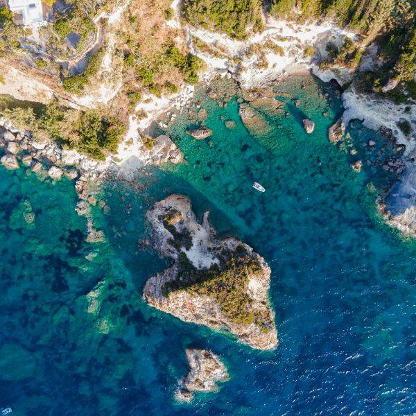 Aerial view of a rocky coastline with turquoise waters and a small boat, symbolizing clarity and exploration.