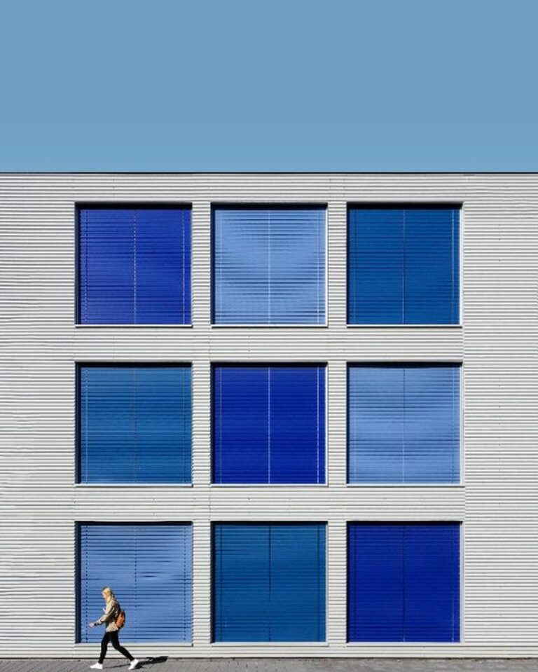 Modern building facade with blue window blinds and a person walking by, illustrating urban life and movement—used in a blog about behavioral activation for depression.