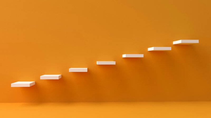 Minimalist image of ascending white steps against an orange background, symbolizing progress and nervous system regulation in therapy.