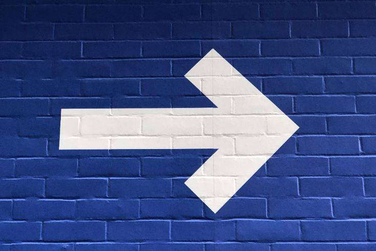 White arrow pointing right on a blue brick wall, symbolizing direction and forward movement.
