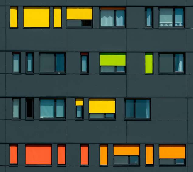 Modern building facade with dark panels and rectangular windows accented by bright yellow, orange, and green panels, symbolizing diversity, creativity, and optimism—key themes of positive psychology.