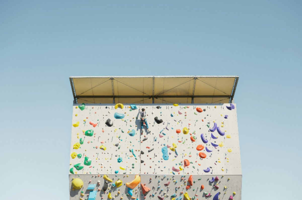 Person climbing a colorful outdoor rock wall under a clear blue sky, symbolizing willpower vs motivation and persistence in achieving goals.