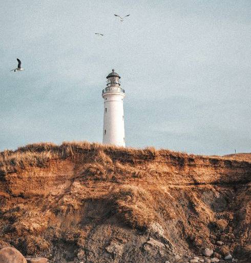 A lighthouse standing on a rocky cliff under a calm sky, symbolizing safety and guidance in uncertain times.