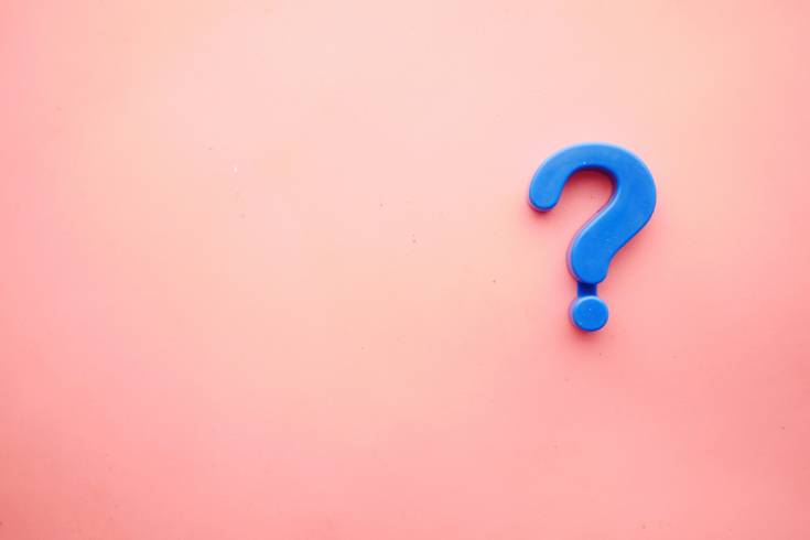 Blue question mark on a soft pink background, symbolizing curiosity and the reflective nature of Socratic questioning in therapy.