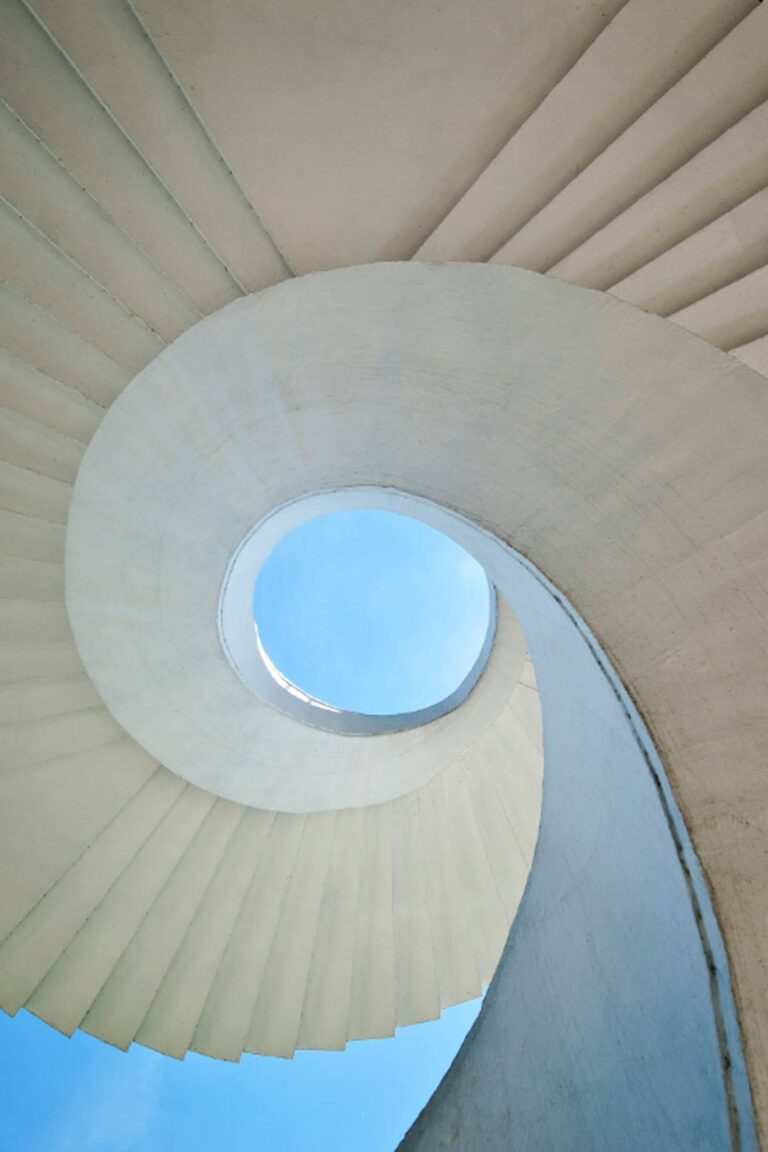 Architectural spiral staircase opening toward the sky, symbolizing the slow, upward reset created by the Mirror–Pause Boundary Technique.