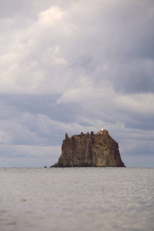A solitary rocky island rising from calm water under a cloudy sky, symbolizing meeting shame with steadiness, curiosity, and compassion.