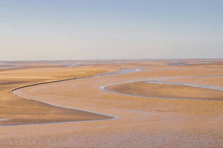 A dry tidal channel winding through sand, shaped by water that once flowed through it.