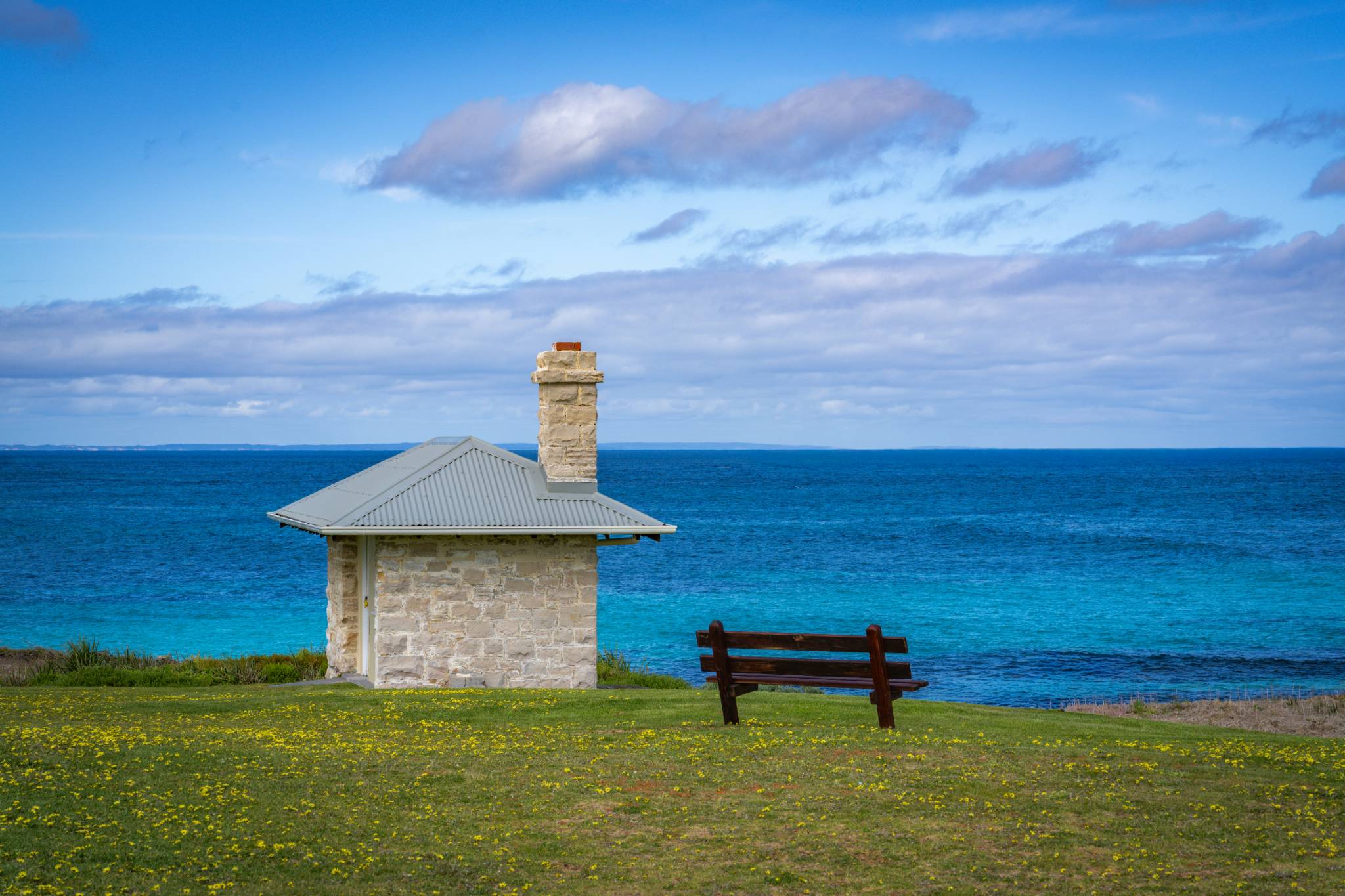 Quiet coastal scene with a single bench overlooking the ocean, reflecting space, calm, and comfort in solitude.