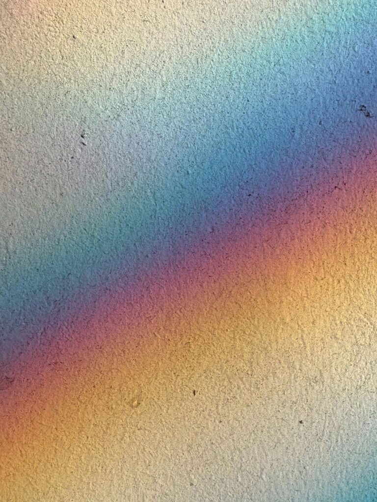 Soft rainbow light reflecting across a textured wall, showing subtle variations in color.