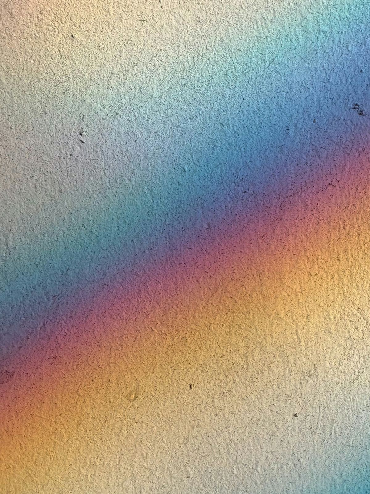 Soft rainbow light reflecting across a textured wall, showing subtle variations in color.